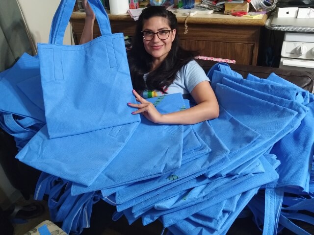 Person surrounded by completed tote bags